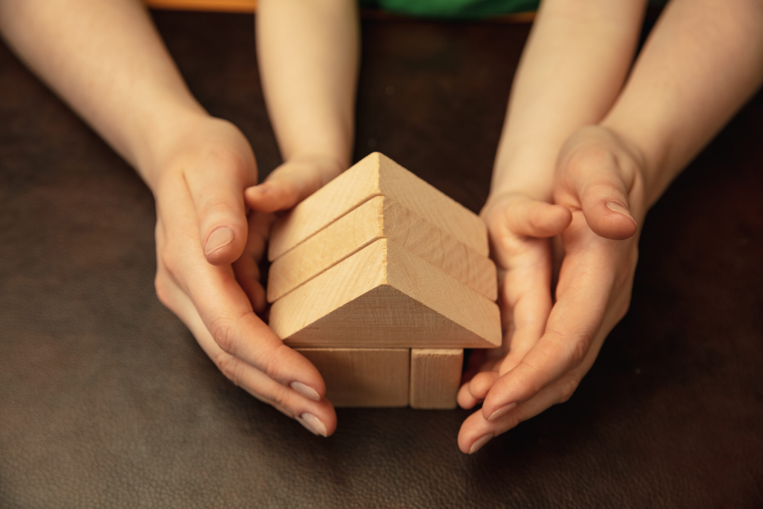 Collecting wooden constructor like house. Close up shot of female and kid's hands doing different things together. Family, home, education, childhood, charity concept. Mother and son or daughter.