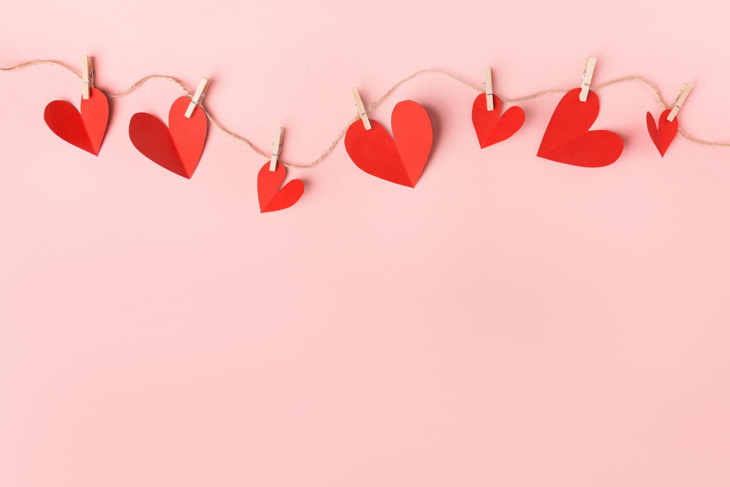 Beautiful valentines day paper hearts hanging on rope on pink background. View from above. Valentines Day Concept.